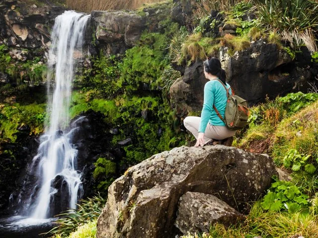 Personne descendant en rappel une paroi rocheuse moussue à côté d'une petite cascade