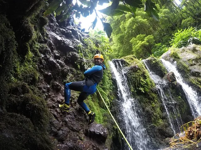 Personne descendant en rappel le long d'une paroi rocheuse couverte de mousse, à côté d'une cascade