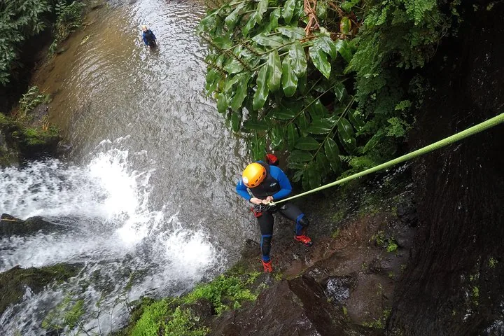 Personne descendant en rappel une falaise à côté d'une cascade impétueuse se jetant dans un bassin