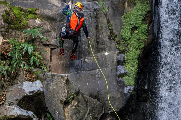 Canyoning-Teilnehmer beim Abseilen an einer felsigen Steilwand neben einem Wasserfall