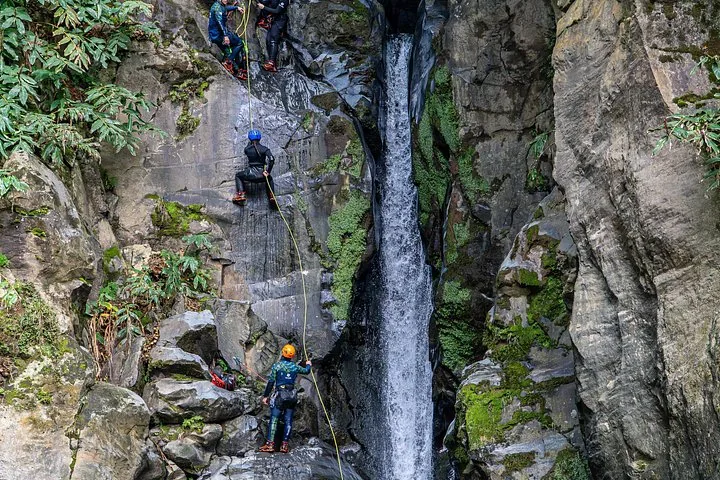People rappelling down a steep rocky cliff beside a tall waterfall